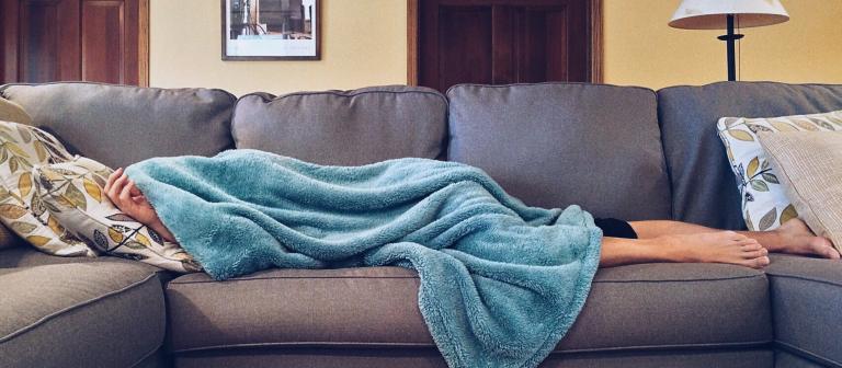 Foto van persoon die op de bank slaapt onder blauwe deken