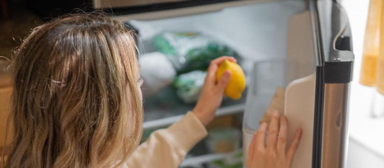 Foto van een vrouw die een citroen uit de koelkast pakt